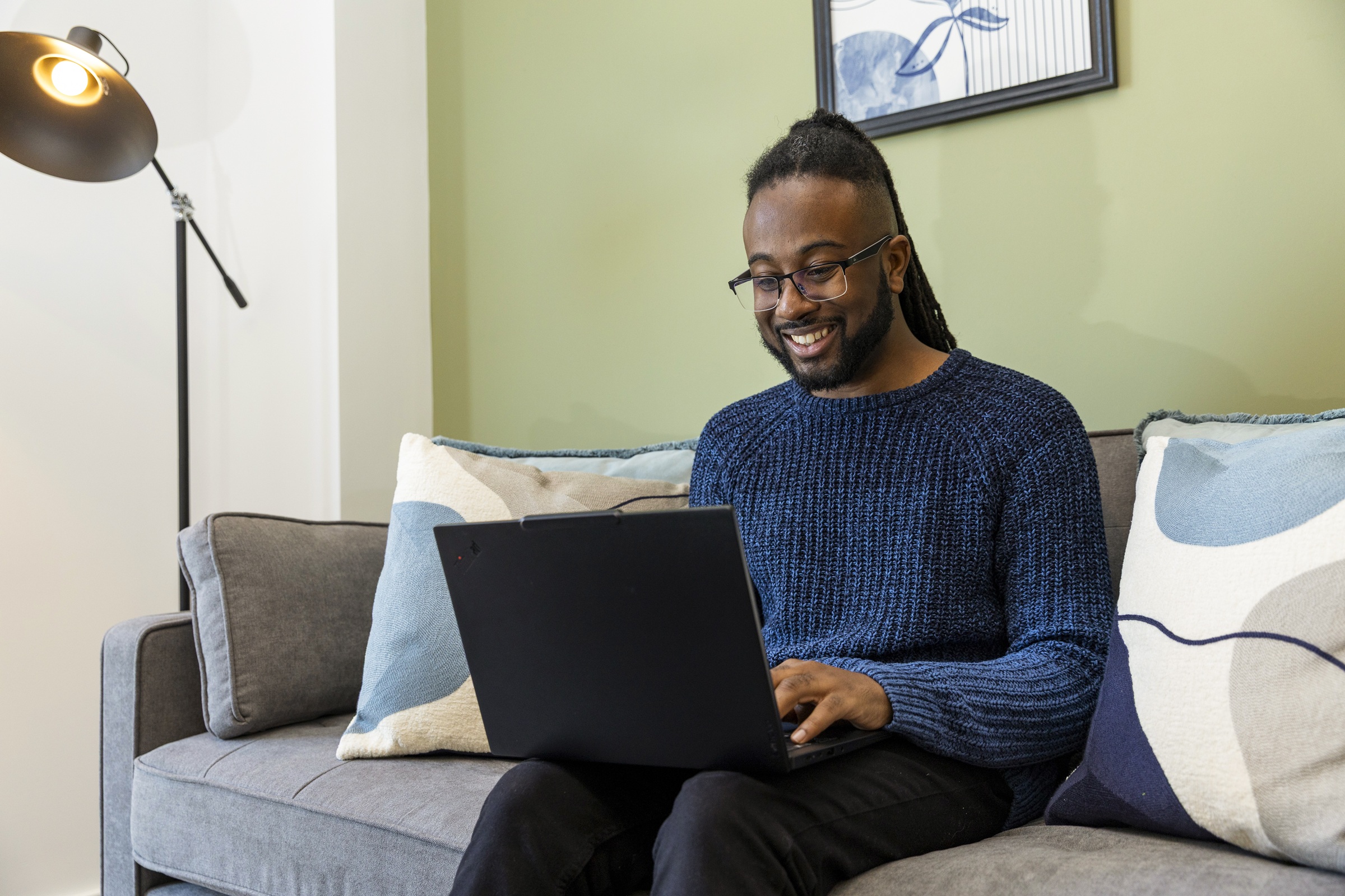 A photograph showing a resident using their laptop whilst sitting on the sofa.