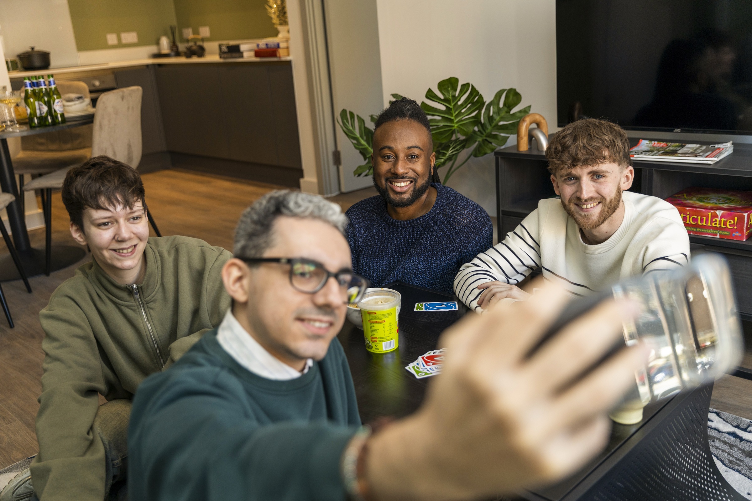 A photograph showing a group of friends posing for a selfie during a card game around the coffee table in the living room.