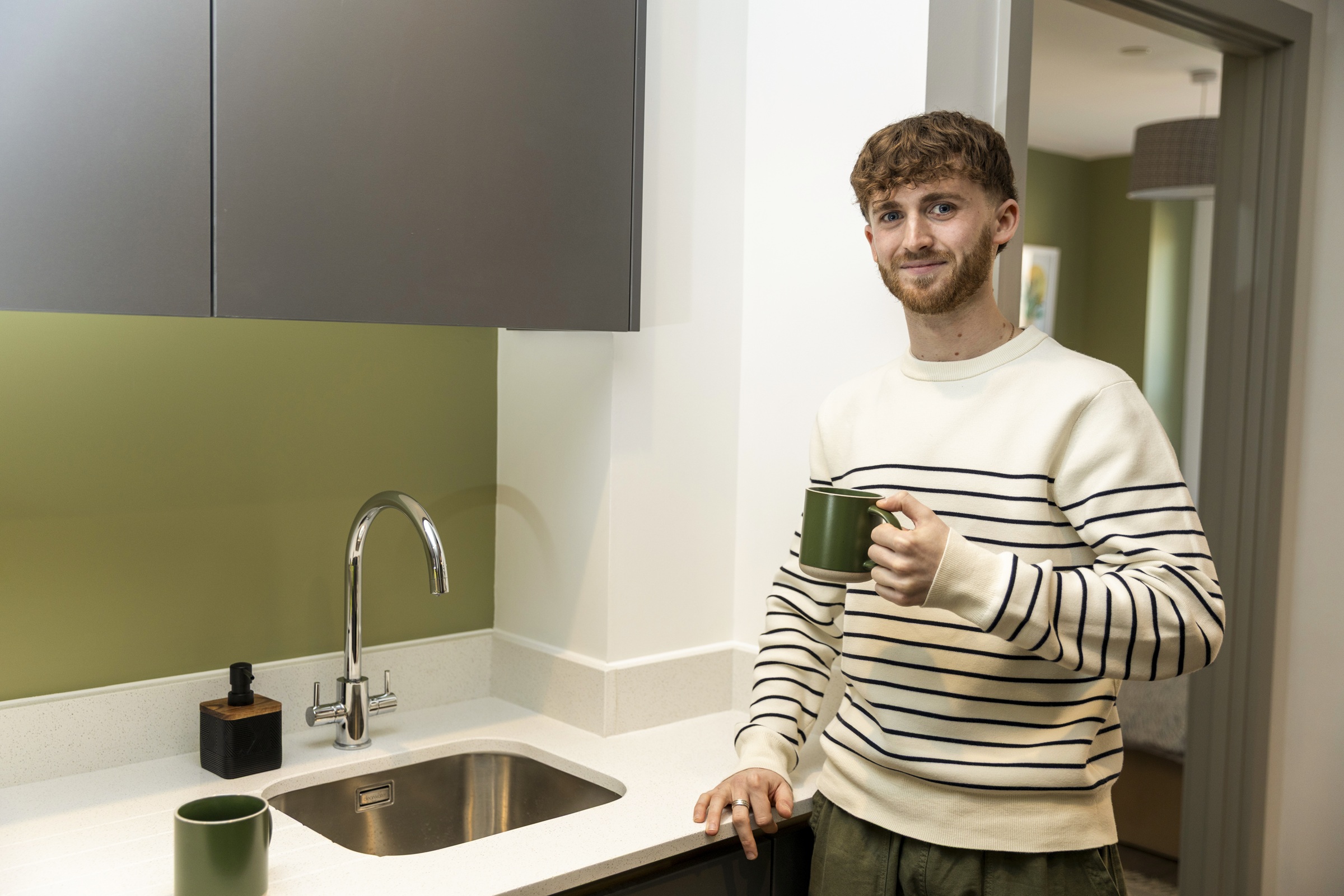 A photograph showing a resident holding a mug by the sink in their kitchen.