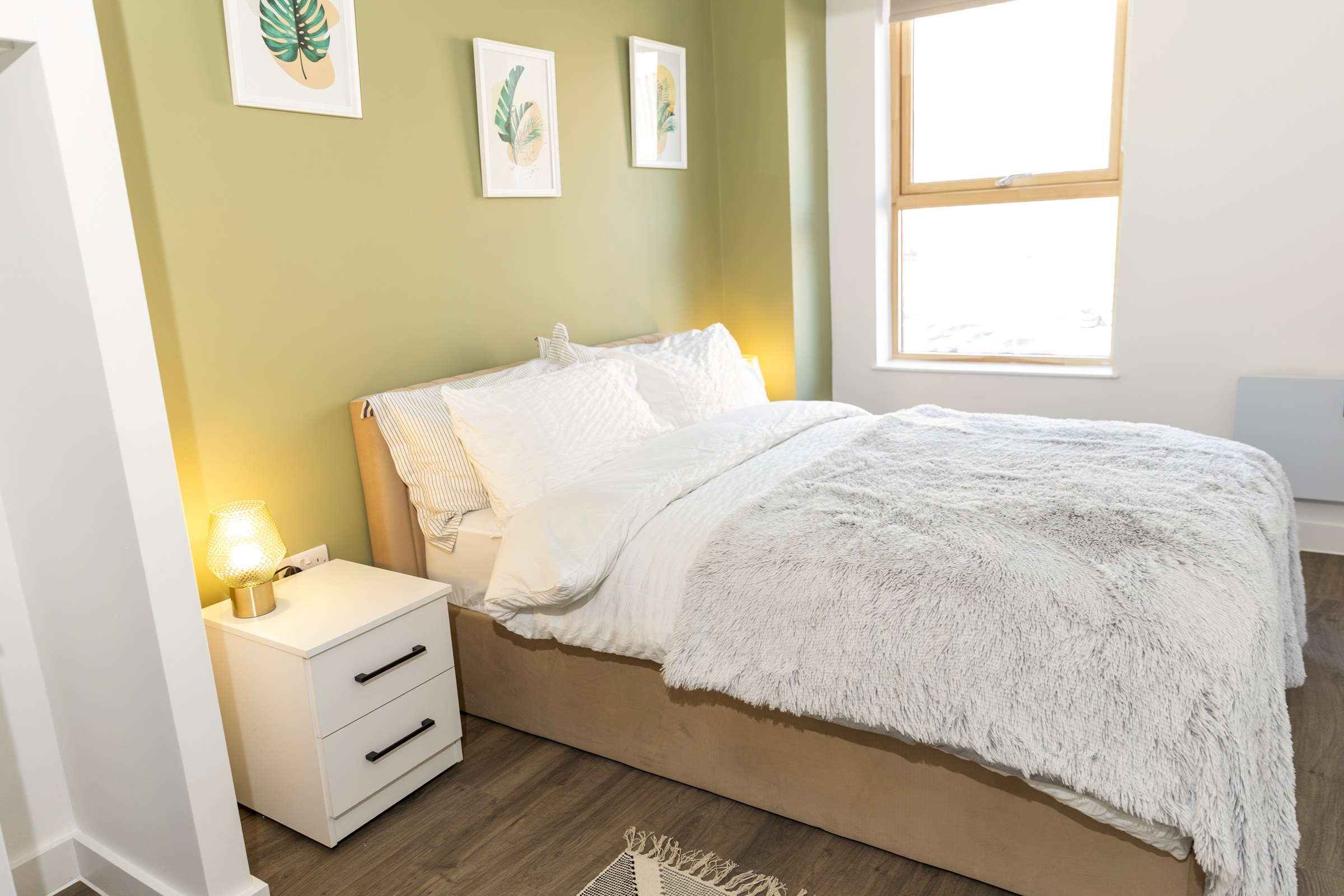 A photograph showing a furnished beroom, including a souble bed, side tables, lamps and wall art.