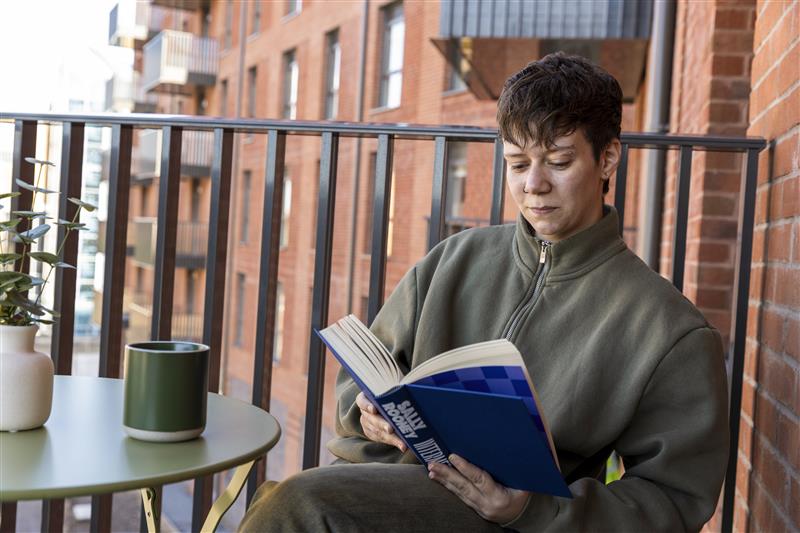 A photograph showing a resident sitting at a table on their private balcony reading a book.