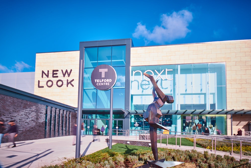 A long exposure photograph showing shoppers outside an entrance to Telford Shopping Centre.